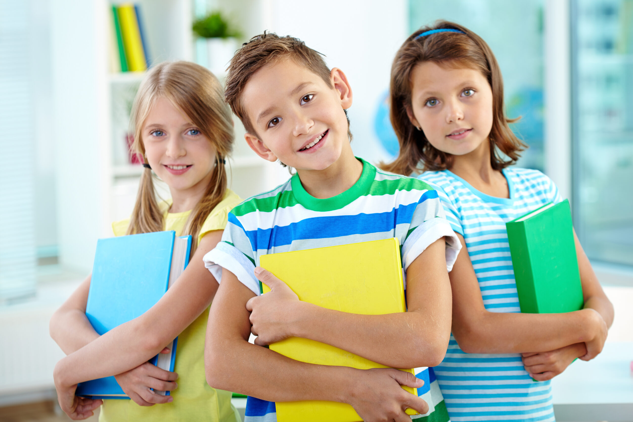 Portrait of happy classmates with books looking at camera in classroom
